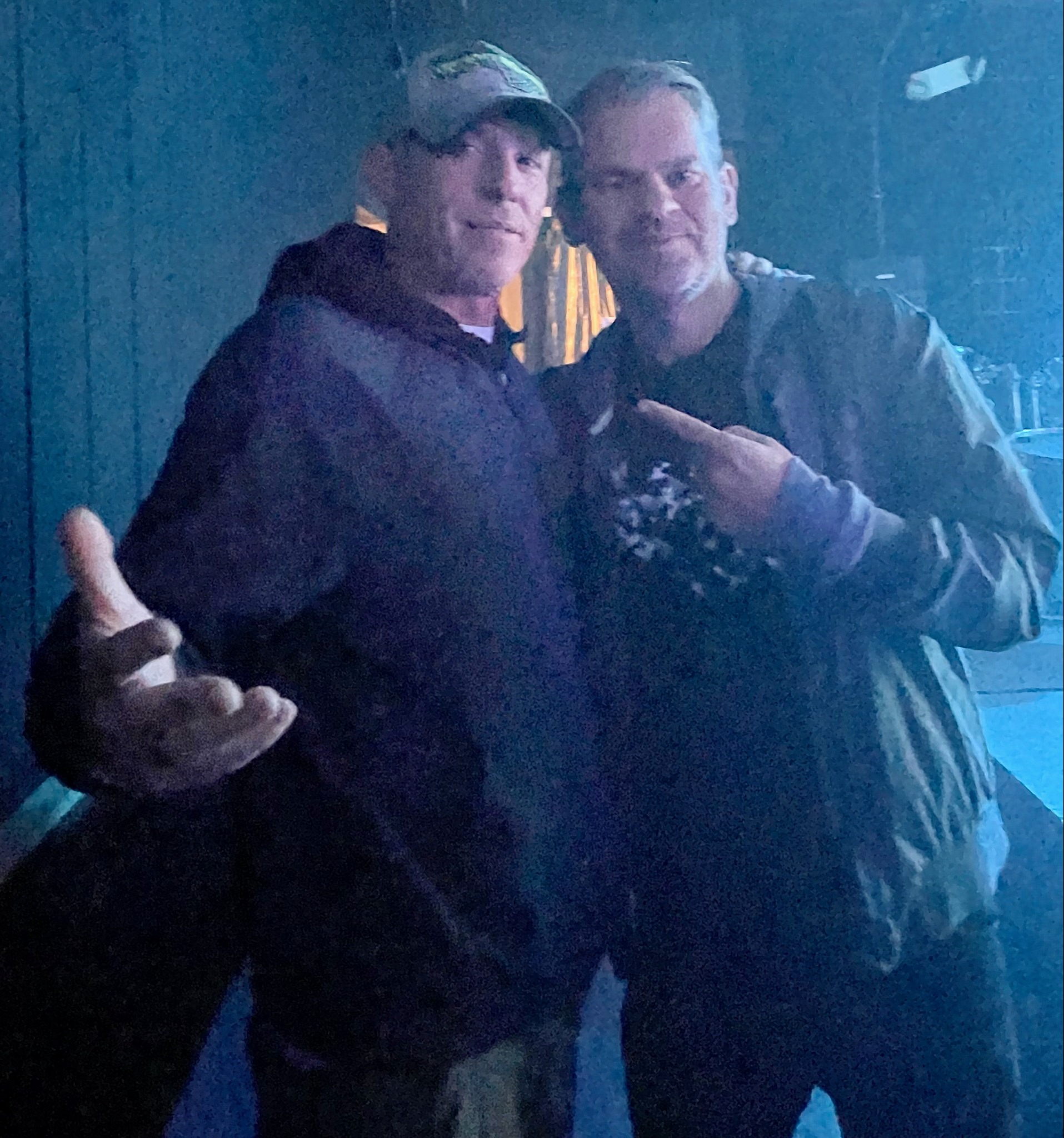 DJ Natural Nate® with a friend backstage under teal blue lighting throwing up hand signs